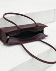 Brown leather handbag with a shoulder strap on a light gray background