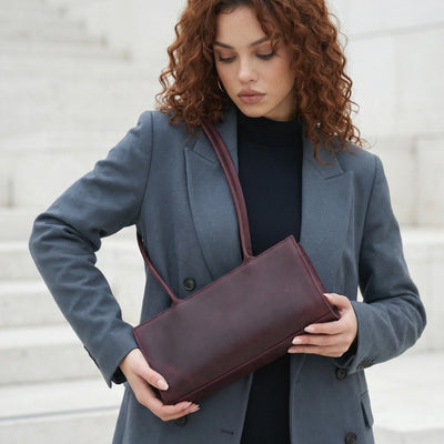 Woman holding a burgundy clutch bag wearing a gray coat.