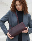 Woman holding a burgundy clutch bag wearing a gray coat.