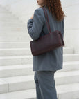 Person in a gray suit with a maroon handbag standing on white steps.