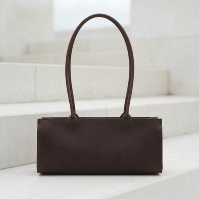 Brown leather handbag on a white surface with a light background