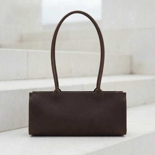 Brown leather handbag on a white surface with a light background