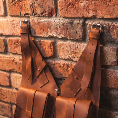 Brown leather suspenders hanging against a brick wall.