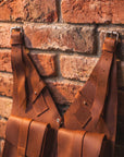 Brown leather suspenders hanging against a brick wall.