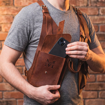 Person wearing a brown leather apron holding a phone with a brick wall background