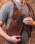 Person wearing a brown leather apron holding a phone with a brick wall background
