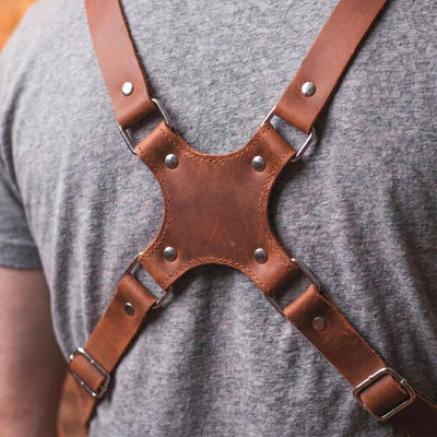 Brown leather harness worn by a person on a gray background
