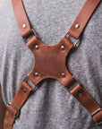 Brown leather harness worn by a person on a gray background