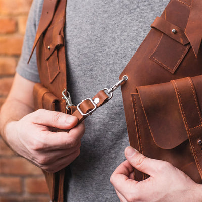 Person adjusting a brown leather bag strap against a brick wall background