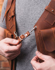 Person adjusting a brown leather bag strap against a brick wall background