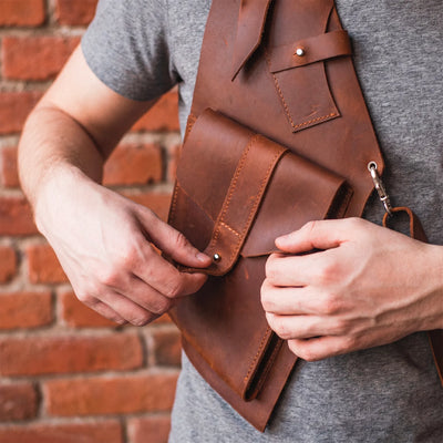 Person holding a brown leather bag against a brick wall